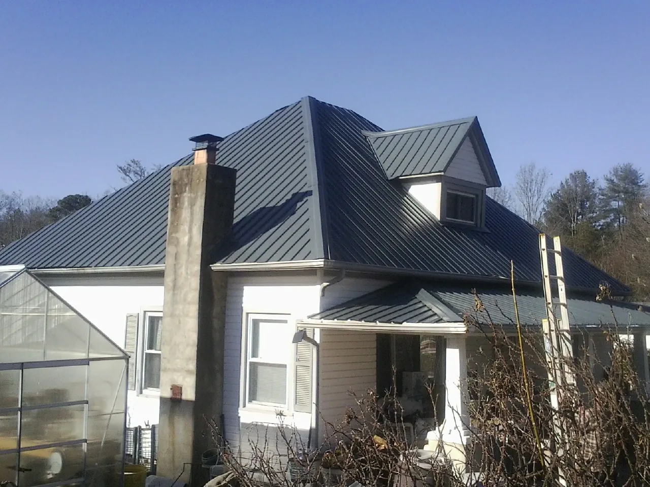 Dark blue standing seam metal roof on a white farmhouse with dormer — Slate & Tile Roof Repair by Roofing Brothers in Raymore