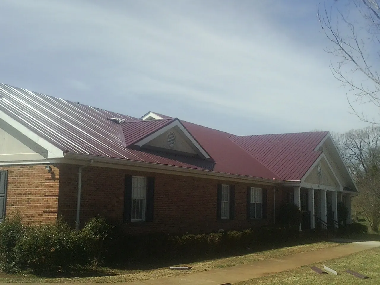 Red metal roof with gabled entries on a long brick building, from a Hail Damage Roof Repair job in Raymore