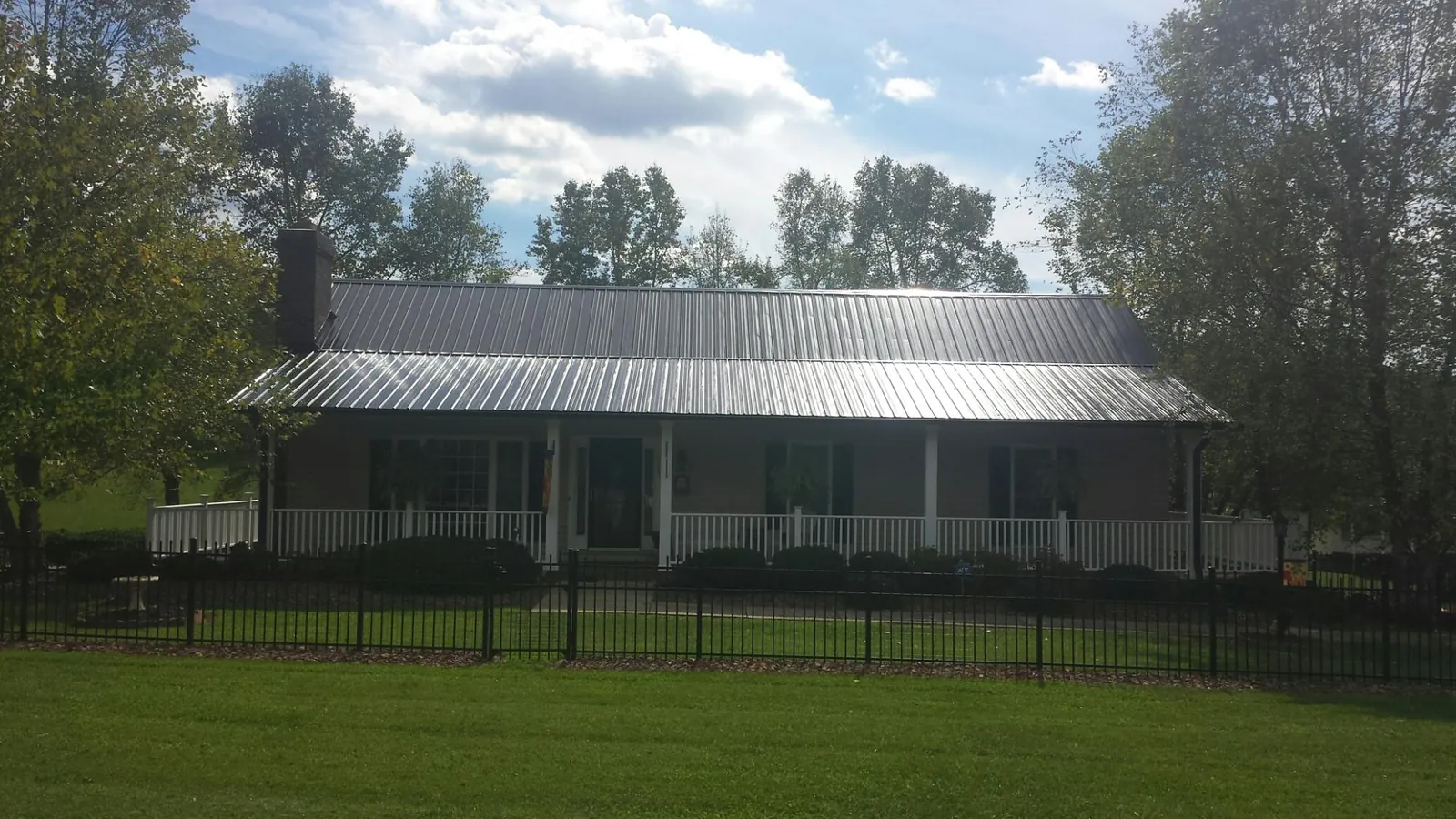 Gray metal roof on a brick ranch with a full width front porch — Gutter Guard Installation work by our crew in Raymore